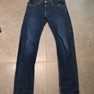 Levi's 512 blå jeans W31 L32 - Säljer ett par klassiska Levi's 512 jeans i mörkblå denim. Modellen har en slim passform med raka ben och fem fickor. Jeansen har snygga kontrastsömmar och klassisk Levi's-lapp bak i midjan. Perfekta för dig som gillar en tidlös och clean look.