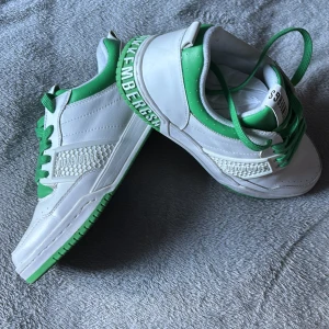 Vita och gröna Bikkembergs sneakers - Snygga sneakers från Bikkembergs i vitt och grönt med coola detaljer och gröna skosnören. Skorna har en tydlig logga på sidan och bak på sulan, samt mönstrad panel på sidan. Perfekta för dig som vill sticka ut med en sportig vibe.