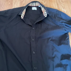 Burberry skjorta - Svart Burberry skjorta i väldigt bra skick. Fick i present men använt bara 3 gånger. Skjortan passar både M/L. Skriv om ni undrar något.