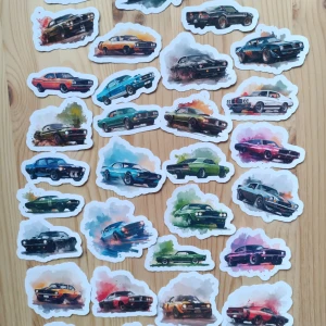 32 klistermärken  - biilar - Bilden visar ett antal klistermärken med motiv av klassiska bilar i olika färger och stilar, placerade på ett träbord. Ingen elektronikprodukt syns på bilden.