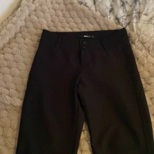 Svarta bootcut kostymbyxor Gina Tricot - Svarta kostymbyxor från Gina Tricot med bootcut-ben och låg midja. Byxorna har två knappar framtill, bälteshällor och bakfickor med knapp. Snygg passform och klassisk look, perfekta till en trendig outfit. Säljer då jag inte längre kan ha de!