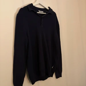 Mörkblå stickad pikétröja Only & Sons - Snygg mörkblå stickad pikétröja från Only & Sons med klassisk krage och knäppning framtill. Tröjan har lång ärm och är perfekt för dig som gillar en stilren och enkel look. Materialet är mjukt och ger en skön känsla.