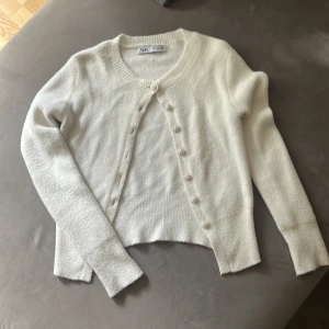 Vit kofta från Zara med pärlknappar - Superfin vit kofta från Zara med långa ärmar och snygga pärlknappar framtill. Koftan är stickad och har en mjuk, fluffig känsla. Perfekt för lager-på-lager och ger en clean look till din outfit. Lagad på baksidan av  mudden längst upp, inget som syns när man har den på.