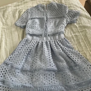 Ljusblå spetsklänning med kort ärm - Superfin ljusblå klänning med kort ärm och rund hals. Klänningen har ett vackert hålmönster i spets och markerad midja. Kjolen är utställd och har flera dekorativa band. Perfekt för dig som gillar romantisk och söt stil!