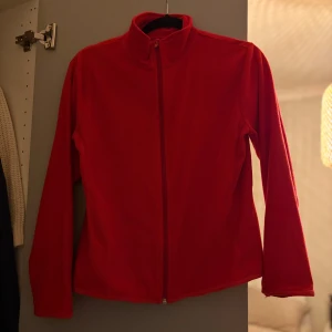 Röd fleecejacka från H&M - Röd fleecejacka från H&M med hel dragkedja och hög krage. Jackan är enkel och stilren med långärmad passform och mjukt fleecematerial som håller dig varm. Perfekt för lager-på-lager under kyliga dagar.