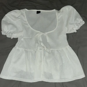 Vit blus med puffärm från Gina Tricot - Supersöt vit blus från Gina Tricot med puffiga korta ärmar och knytning framtill. Blusen har en lätt rynkad struktur. 