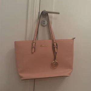 Rosa handväska från Schulzignac - Snygg rosa handväska från Schulzignac med justerbara axelremmar och guldfärgade detaljer. Väskan har ett stort huvudfack med flera innerfickor, varav en med dragkedja. Perfekt för att få plats med allt du behöver och samtidigt hålla stilen.