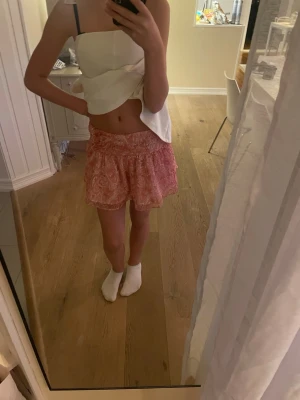 Rosa kortkjol med paisleymönster - Säljer en söt rosa kortkjol med paisleyinspirerat mönster. Kjolen har volangdetaljer och är gjord i ett lätt och luftigt material som känns skönt mot huden. Perfekt för dig som gillar färg och mönster! Passformen är normal och midjan är elastisk.