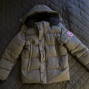 Canada Goose Jacka  -  Canada Goose med huva och klassisk logga på ärmen. Perfekt för kalla dagar och har en riktigt schysst look.