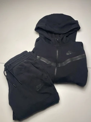 Nike tech fleece set  - Säljer ett svart Nike Tech Fleece set (hoodie och byxa). Snygg och skön passform och lätt att styla. Har snygga detaljer och praktiska fickor, huva, dragkedja och Nike logotypen. Säljer på grund av att det inte passar mig. Priset är inte hugget i sten!