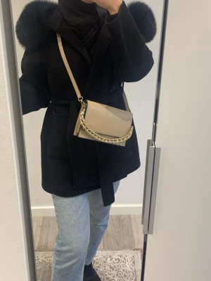 Svart kappa med päls - Säljer en svart kappa med stor fluffig päls på luvan och ett bälte i midjan. Jackan har en klassisk och stilren look, perfekt för dig som vill ha något snyggt och varmt. Långärmad och med snygg krage. Använd enbart två gånger och är som ny. Passar både 34/36