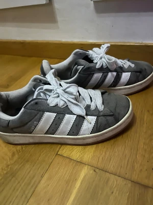 Grå Adidas Campus sneakers🩶🩶 - Säljer ett par grå Adidas Campus sneakers med klassiska vita ränder på sidorna och vit sula. Skorna har rund tå, snörning och är gjorda i mocka med textilfoder. Perfekta för dig som gillar retrostil och vill ha något bekvämt till vardags.