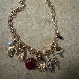 Halsband - Bilden visar ett halsband med olika berlocker, bland annat snäckor, fisk och pärlor. Ingen väst finns på bilden.