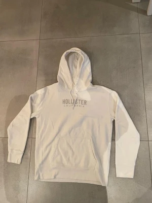 Vit hoodie från Hollister  - Snygg vit hoodie från Hollister, (bland de mest eftertraktade just nu) mycket bra skick med inga defekter, storleken är M och sitter bra på killen som är ca 185. Hör av dig vid minsta lilla, MVH EM_RESELL 