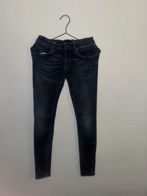 Mörkblå skinny jeans från T/J - Snygga mörkblå skinny jeans från T/J med klassisk femficksdesign och ljusa slitningar framtill. Jeansen har låg midja och smal passform som sitter tight längs benen. Materialet är stretchigt jeans för extra komfort och rörelsefrihet.