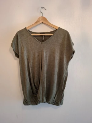 Olivgrön blus från Rainbow - Säljer en olivgrön blus från Rainbow i storlek 36/38. Toppen har v-ringad hals, korta ärmar och ett snyggt draperat parti nedtill. Materialet är mjukt och lätt, perfekt för vår och sommar. Enkel och stilren design som funkar till många olika looks.