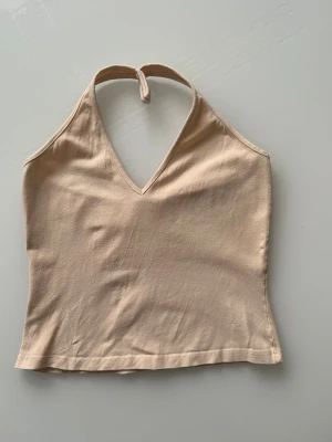 Beige halterneck linnetopp från H&M - Säljer en stilren beige halterneck linnetopp från Hennes collection. Toppen har v-ringad hals och knyt i nacken, vilket ger en snygg och enkel look. Materialet känns mjukt och lätt, perfekt för varma dagar. Passar dig som gillar minimalistisk stil.