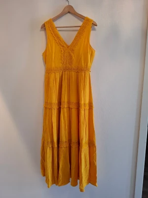 Gul långklänning från KappAhl S - Säljer en solgul långklänning från KappAhl i storlek S. Klänningen har v-ringning, breda axelband och fina spetsdetaljer längs urringning och midja. Tillverkad i ett lätt, luftigt material med volang och struktur i tyget. Perfekt för varma dagar!