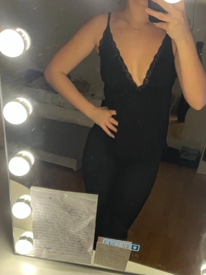 Svart spetsdetaljerad linnetopp - Säljer en svart linnetopp med djup v-ringning och tunna axelband. Toppen har fina spetsdetaljer längs ringningen som ger en extra touch. Köpt från Nelly i mycket gott skick.