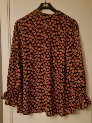 Blommig blus med volang på ärmarna  - Jättefin blus med rosa rosor mot svart bakgrund. Storlek M från Shein. Knäppning bak i nacken. Mkt fint skick. Kolla gärna in mina andra annonser! 