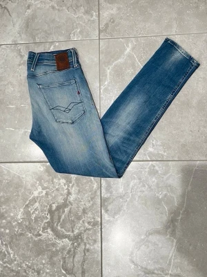 Replay Anbass Hyperflex jeans - Replay Anbass Hyperflex jeans i blå tvätt med snygga slitningar. Jeansen har dragkedja, normal passform och är tillverkade i stretchigt jeansmaterial för extra komfort. Perfekt för dig som gillar stilrena och bekväma jeans. Storleken är i L32 och W30.