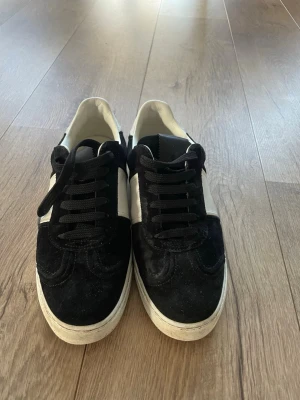 Valentino Garavani svartvita sneakers - Säljer ett par snygga Valentino Garavani sneakers i svart och vitt med coola nitar på sulan. Skorna har snörning, rund tå och är tillverkade i skinn och mocka. Perfekta för dig som gillar stilrena och lyxiga detaljer. OBS saknar 3 nitar 