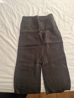 Svarta linnebyxor från Lindex, strl 42 - Säljer ett par svarta linnebyxor från Lindex i storlek 42. Byxorna har rak och lite vidare passform med hög midja och stängs med hakar fram. Materialet är linne som ger en skön och luftig känsla. Perfekt för dig som gillar stilrena och bekväma plagg.