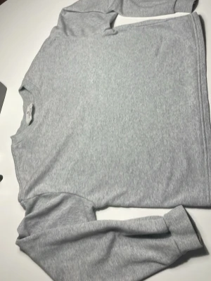 Grå långärmad sweatshirt från H&M - Säljer en enkel och stilren grå sweatshirt från H&M i mjuk bomull. Tröjan har rund hals och långa ärmar, perfekt för chill dagar eller när du vill ha något bekvämt. Passformen är normal och materialet känns skönt mot huden.