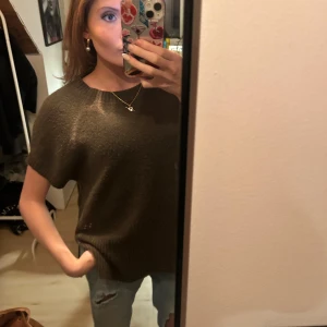 Olive/ khaki grön stickad kortärmad tröja - Säljer en brun stickad tröja med korta ärmar och rund hals. Tröjan har en avslappnad passform och är perfekt att styla med jeans eller kjol. Mjuk och skön, passar bra till lager-på-lager under höst och vår.