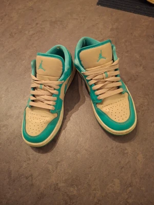 Nike Air Jordan 1 Low Turkos/Vit - Säljer ett par Nike Air Jordan 1 Low i fräsch turkos och vit färg. Skorna har klassisk snörning, perforerad tåbox och ikoniska Jordan-loggor på plös och häl. Tillverkade i skinn med kontrasterande detaljer och låg profil. Perfekta för dig som vill sticka ut.