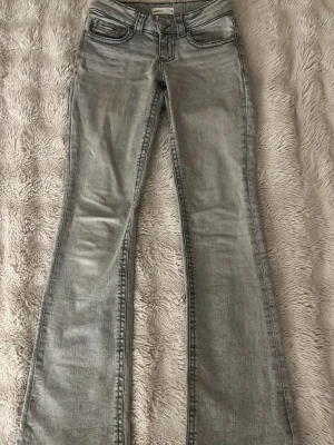 Bootcut grå jeans från Gina Tricot - Snygga grå bootcut jeans från Gina Tricot i storlek 32. De har klassisk femficksdesign, bälteshällor och dragkedja med knapp. Jeansen har en cool tvättad look och är tillverkade i mjukt jeanstyg som sitter skönt hela dagen.