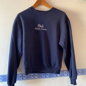 Mörkblå sweatshirt från Polo Ralph Lauren - Snygg mörkblå sweatshirt från Polo Ralph Lauren med broderad logga på bröstet. Tröjan har långa ärmar och ribbade muddar vid ärmslut och nederkant. Perfekt för en avslappnad stil. Fint skick, dock alla lappar inuti bortklippta, därav lågt pris 