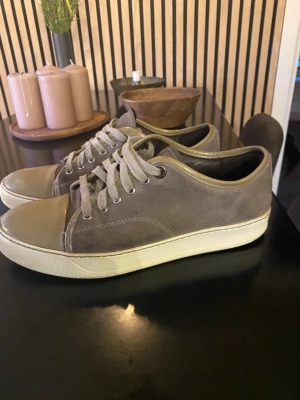 Gröna lanvins med mockadetaljer - Säljer ett par gröna sneakers från Lanvin med snygga mockadetaljer och olivgrönt tåparti. Skorna har rund tå, snörning och vit platt sula. Perfekt för dig som gillar stilrena och neutrala färger. Passar till många olika outfits och har en klassisk look. FINNS INGEN KARTONG TILL.