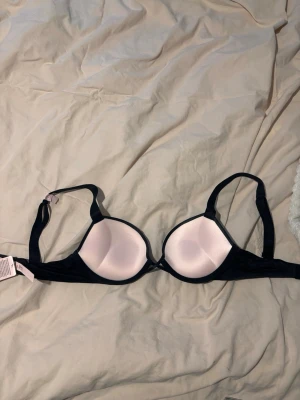 Svart och ljusrosa bh Victoria's Secret - Säljer en snygg bh från Victoria's Secret i svart med ljusrosa kupor. Bh:n har justerbara axelband och klassisk form med släta kupor. Den är endast provad 1!gång lapp å allt sånt kvar nypris 900+