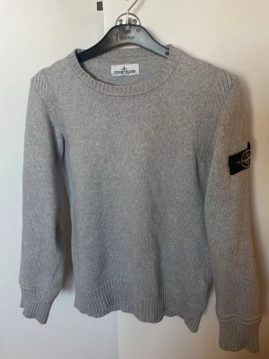 Stickad Stone Island tröja (äkta) - Säljer en grå stickad långärmad tröja från Stone Island med crewneck. Tröjan har den klassiska logotyp-patchen på vänster ärm och en väldigt snygg design. Tröjan är värderad till ett nypris på 2000-3000kr. Säljer på grund av att den inte passar mig. Extra knappen medföljer. Priset är inte hugget i sten!