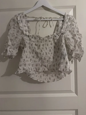Vit blommig blus med puffärm - Säljer en söt vit blus från H&M i storlek M med små blommor i lila och grönt. Blusen har puffiga korta ärmar, smockad kropp och volangdetaljer vid hals och nederkant. Knytband i nacken och fyrkantig ringning. Använd nån enstaka gång så i mycket bra skick 😁