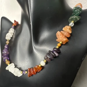 Vintage boho halsband med äkta råslipade ädelstenar – Ametist, Rosenkvarts, Karneol & Obsidian mm - Retro - 70-tals vibe - Hippie  - Vintage halsband med råslipade halvädelstenar i flera färger, kombinerat med mässingsfärgade mellandelar och klassiskt skruvlås. Stenarna inkluderar bland annat ametist, rosenkvarts, aventurin, karneol och obsidian – varje sten har sin egen naturliga form och energi.  Halsbandet är ett auktionsfynd & i mycket fint skick. Perfekt för dig som gillar bohemisk, etnisk och naturinspirerad stil.   Längd ca 50 cm. Priset är redan lågt – så jag prutar inte, men jag ger mängdrabatt vid köp av fler saker.