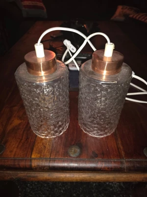 Fönsterlampor - Bilderna visar två lampor med kopparfärgad topp och strukturerat glas, samt vit sladd. Ingen väst syns på bilderna. Medföljer inte lampor. Mått på dem är Höjd 16.5 cm och öppningen nedtill 10.5 cm