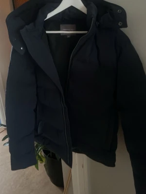 Mörkblå pufferjacka från Lawrence Grey/ peak performance ljus blås storlek L passar både m och s liten i storleken  - Säljer en mörkblå pufferjacka från Lawrence Grey i storlek M. Jackan har huva med tryckknappar och dragkedja framtill. Perfekt för kalla dagar och har en clean, stilren look som funkar till många outfits. Och en peak performance jacka i storlek L men liten i storlek så passar som både M/S
