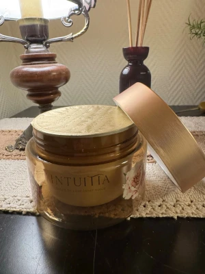 Intuiita body cream - Body cream från Intuiita i en lyxig, rund glasburk med guldfärgat lock och blommig dekor. Innehåller vaniljessens som ger en fräsch och mjuk känsla till huden. Perfekt att spraya för extra återfuktning och glow.