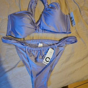 Ljuslila bikini från cubus, storlek L - Superfin ljuslila bikini från cubus i storlek L. Bikinin har draperade detaljer, samt klassisk bikiniunderdel med resår i midjan. Materialet är återvunnen polyamid som ger en mjuk och glansig finish. Perfekt för stranden eller poolen!