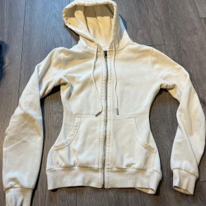 Skräddarsydd hoodie  - Vit hoodie från H&M Basics med huva och snörning, hel dragkedja framtill och två fickor. Mjuk bomullskänsla och ribbade muddar vid ärmslut och nederkant. Perfekt för chill dagar eller när du vill ha en enkel och clean look.