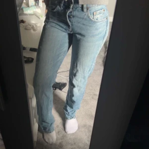 Ljusblå raka jeans från Zara - Säljer ett par ljusblå jeans från Zara med raka ben och klassisk femficksdesign. Jeansen har hög midja och stängs med knappar. Tillverkade i jeansmaterial med en snygg tvättad look. Perfekta för en avslappnad och trendig stil.