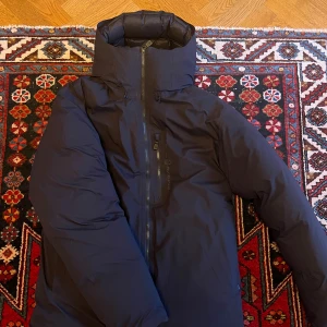 Svart dunjacka Sail Racing Black Ice - Säljer en svart dunjacka från Sail Racing, modell Black Ice med GORE-TEX. Jackan har hög krage, dragkedja framtill och diskret logga på bröstet. Fodret är glansigt och jackan är riktigt puffig och varm, perfekt för kalla dagar. Jackan är använd max 2 gånger!