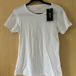 Vit basic t-shirt från  - En klassisk vit t-shirt från Take Off med rund hals och korta ärmar. Tillverkad i mjuk bomull för en skön känsla. Perfekt att matcha med jeans eller shorts för en clean och enkel stil. Inte använd så prislappen är kvar.