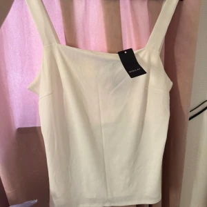 Vit ribbad linnetopp  - Säljer en stilren vit linnetopp  med breda axelband och ribbad struktur. Toppen har rak halsringning och ärmlös design, perfekt för att matcha med jeans eller kjol. Enkel och fräsch look för sommaren.