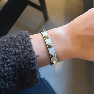 Valentino Garavani Rockstud armband - Coolt armband från Valentino Garavani i ljusbeige skinn med ikoniska pyramidformade nitar i guld. Justerbart spänne med logga och stilren design som ger en edgy vibe. Kommer med originalpåse och box från Valentino.