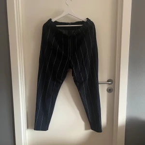 Svarta randiga byxor från ONLY - Svarta byxor från ONLY med vita vertikala ränder och elastisk midja. Modellen är taperedi med normal passform och har fickor bak. 