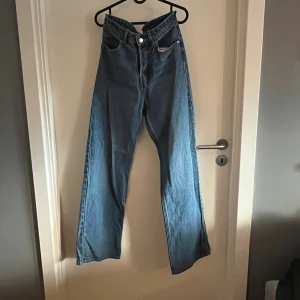 Blå wide jeans från HM - Säljer ett par blå jeans från HM i storlek 34. Modellen har hög midja och raka, vida ben. Klassisk femficksdesign och knappstängning framtill. 