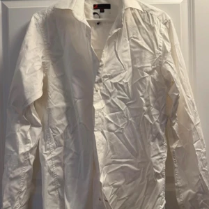 Vit skjorta från Dressmann, M - Klassisk vit skjorta från Dressmann i storlek M med krage och långa ärmar. Skjortan har knappar framtill och är tillverkad i mjukt bomullstyg. Perfekt för dig som gillar stilrena och enkla plagg med snygg passform.